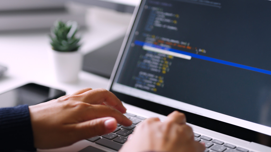 Close-up of hands typing JavaScript code on laptop during Pitman Training IT Specialist course