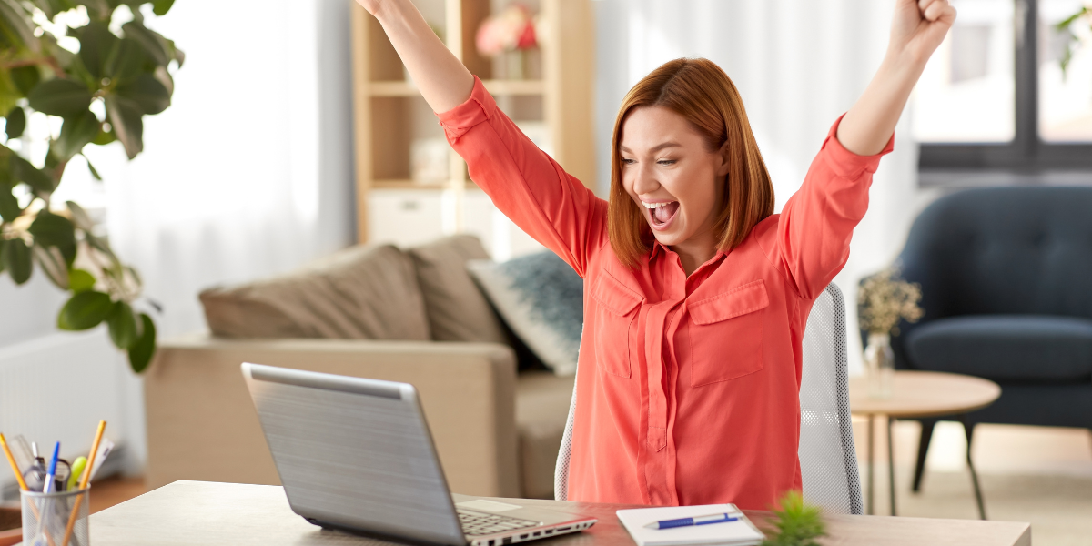 A woman celebrates with raised arms at her home office desk after successfully following her guide to returning to work