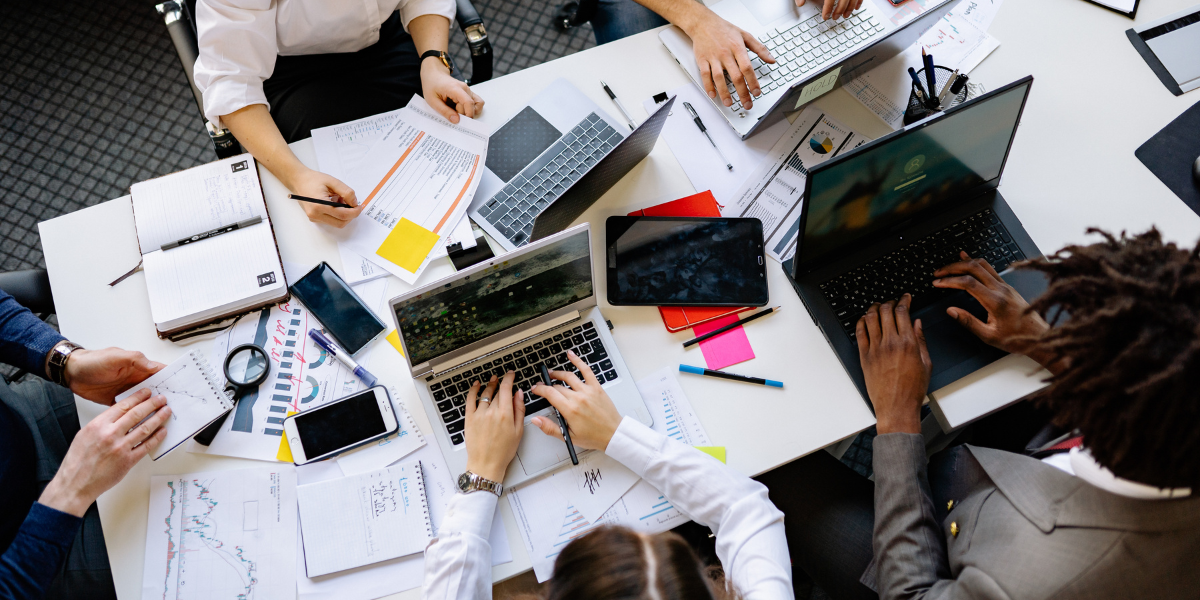 Business professionals collaborating at a meeting table with laptops and financial documents, discussing workplace policies including UK minimum wage regulations that affect employee compensation and business operations.